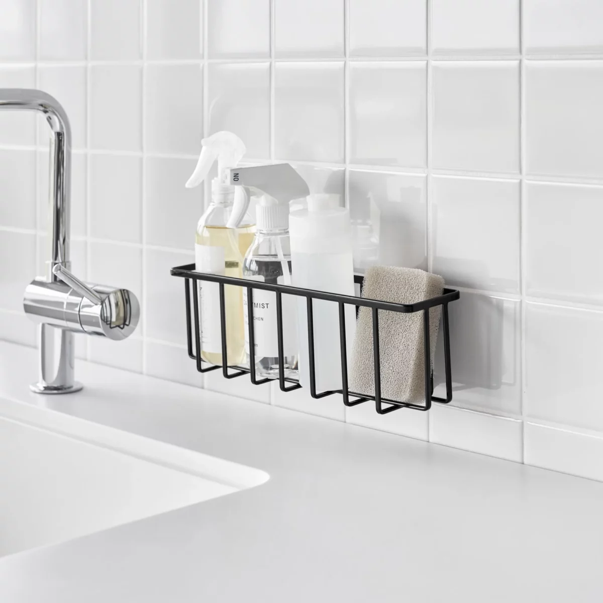 Yamazaki TOWER Film Hook multi-use basket L in black, on a tiled wall next to the sink with spray bottles