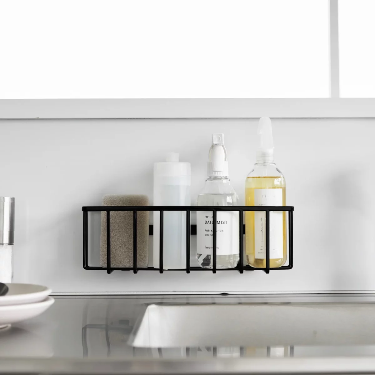 Yamazaki TOWER Film Hook multi-use basket L in black, front view on the wall with bottles and a brush