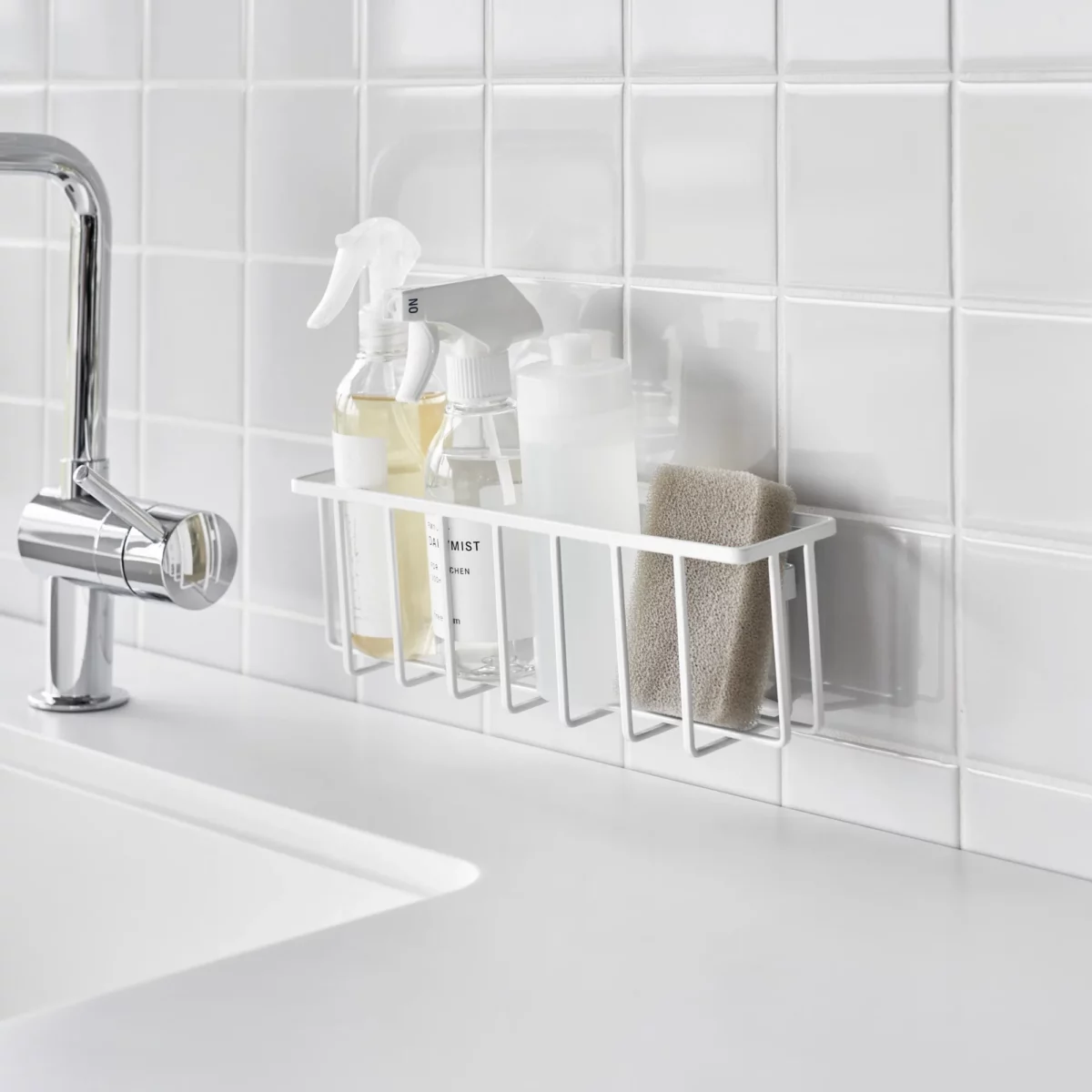 Yamazaki TOWER Film Hook multi-use basket L in white, on a tiled wall next to the sink with spray bottles