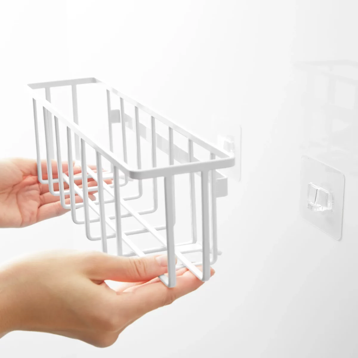 Yamazaki TOWER Film Hook multi-use basket L in white, hands placing the basket onto the adhesive hook