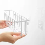 Yamazaki TOWER Film Hook multi-use basket L in white, hands placing the basket onto the adhesive hook
