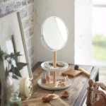 Yamazaki TOSCA makeup mirror with shelves in white, on the vanity next to the makeup brushes and alarm clock