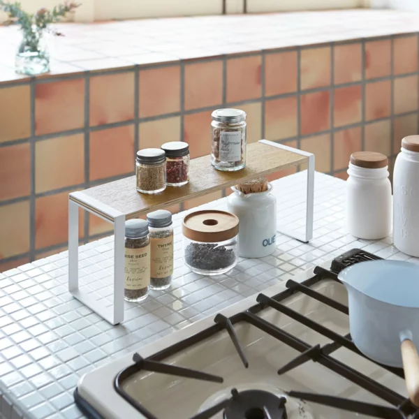 Étagère de cuisine Yamazaki TOSCA, large, en blanc, placée à côté de la cuisinière à gaz, avec des bocaux à épices disposés sur deux niveaux
