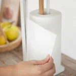 Yamazaki Küchenrollenhalter TOSCA in Weiss, Hand zieht ein Blatt Küchenpapier am Bügel vorbei