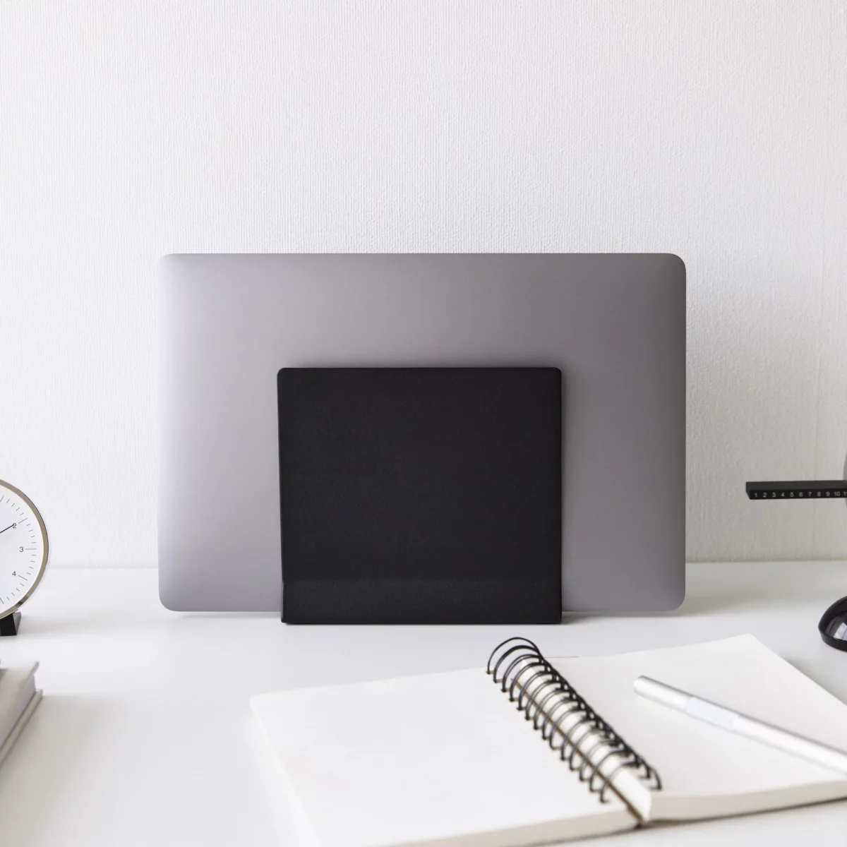 Support pour ordinateur portable Yamazaki TOWER vertical, noir, vu de face sur le bureau avec un bloc-notes