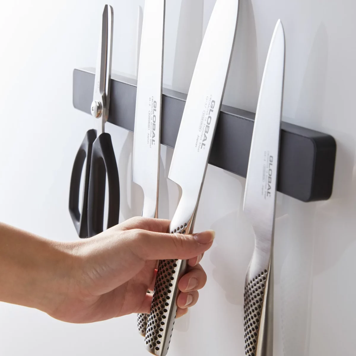 Yamazaki TOWER Magnetic Knife Rack in Black; a hand picks up a knife from the rack