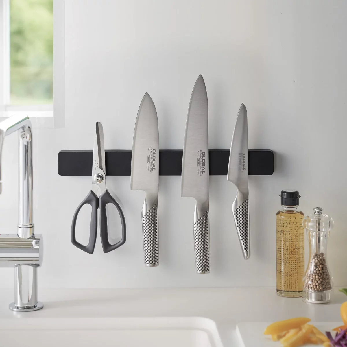 Yamazaki TOWER Magnetic Knife Rack in Black, above the sink with knives next to the oil and pepper shakers