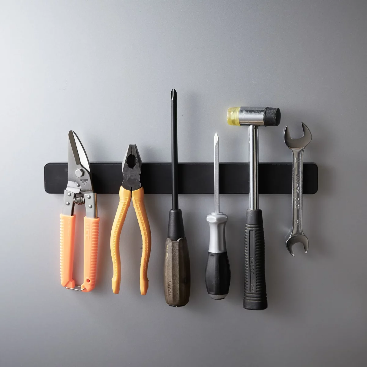 Yamazaki TOWER Magnetic Knife Rack in Black, with pliers, screwdriver, and hammer on a gray wall