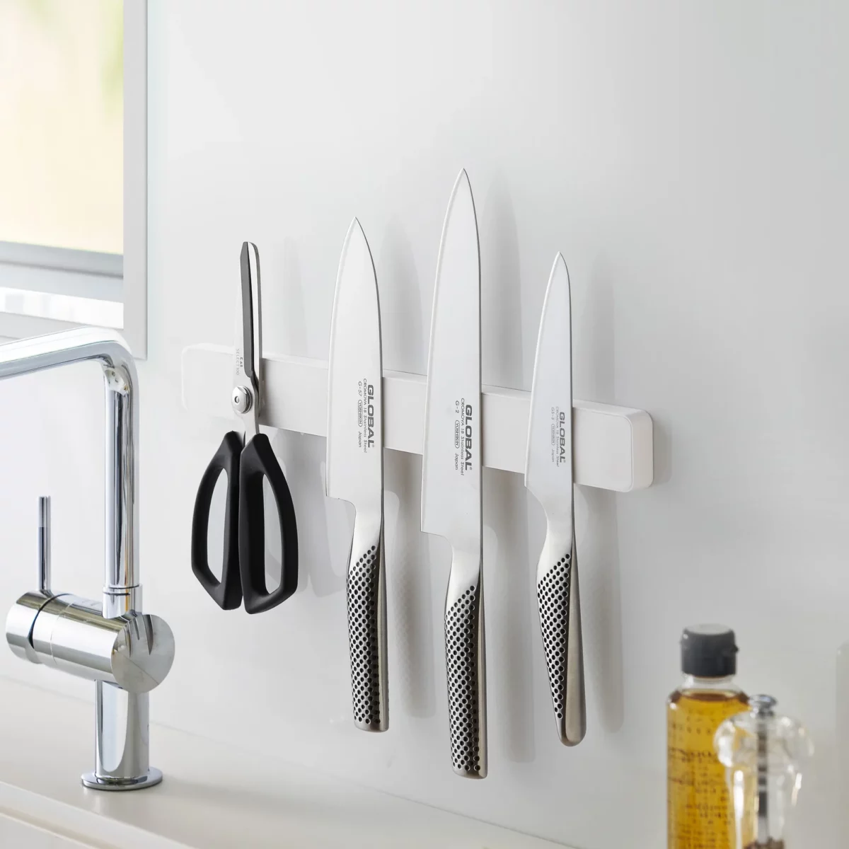 Yamazaki TOWER Magnetic Knife Rack in White, mounted on the kitchen wall with three knives and a pair of scissors
