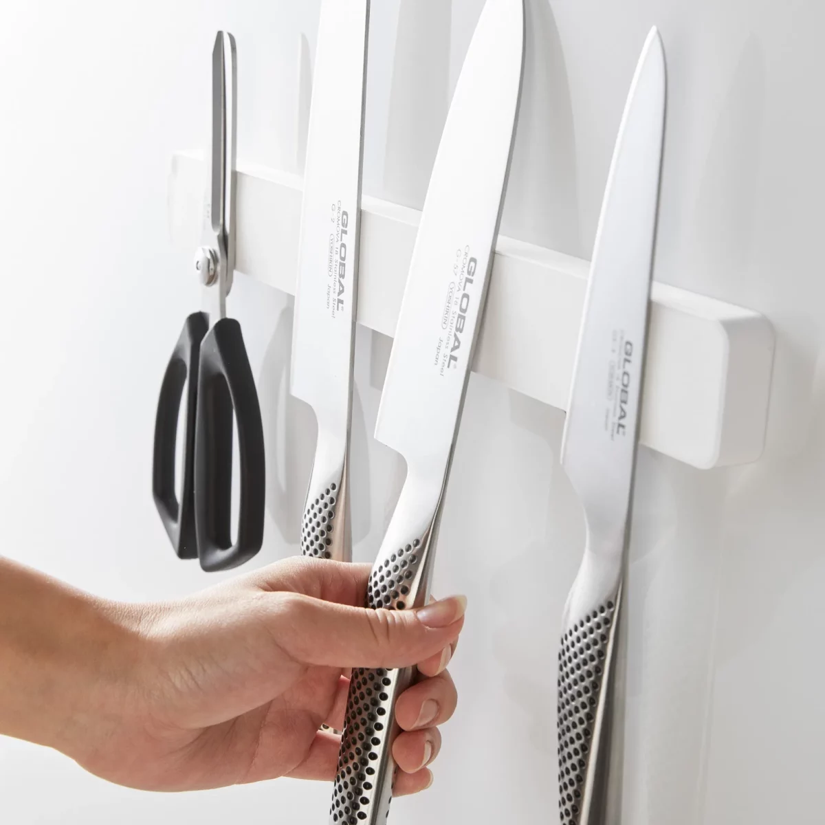 Yamazaki TOWER Magnetic Knife Rack in White; a hand picks up a knife from the rack