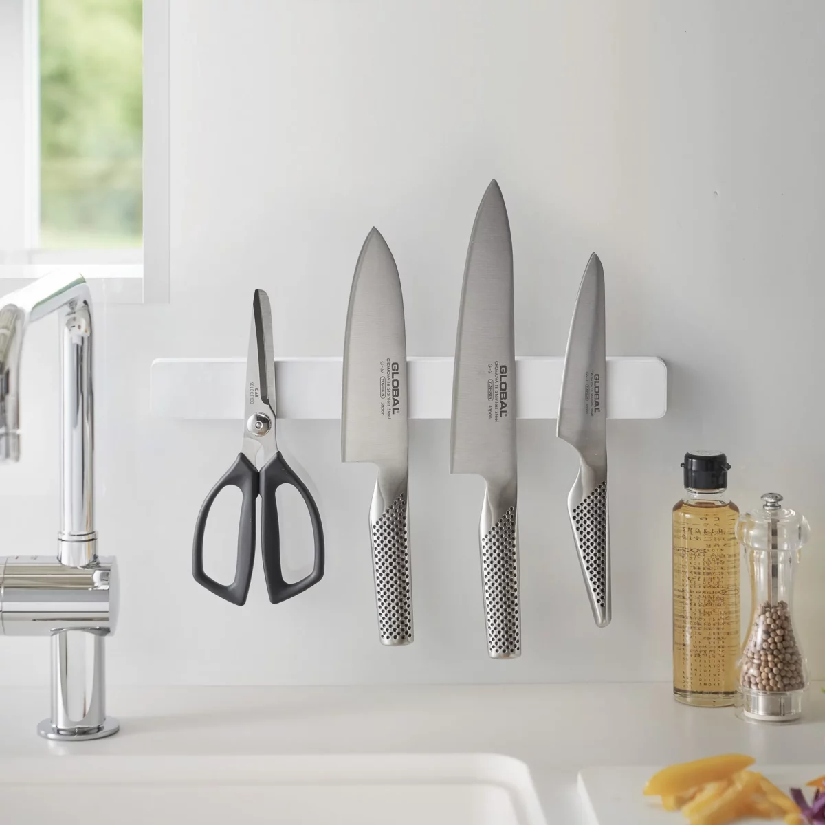 Yamazaki TOWER Magnetic Knife Rack in White, mounted above the sink with knives next to the oil and pepper shakers