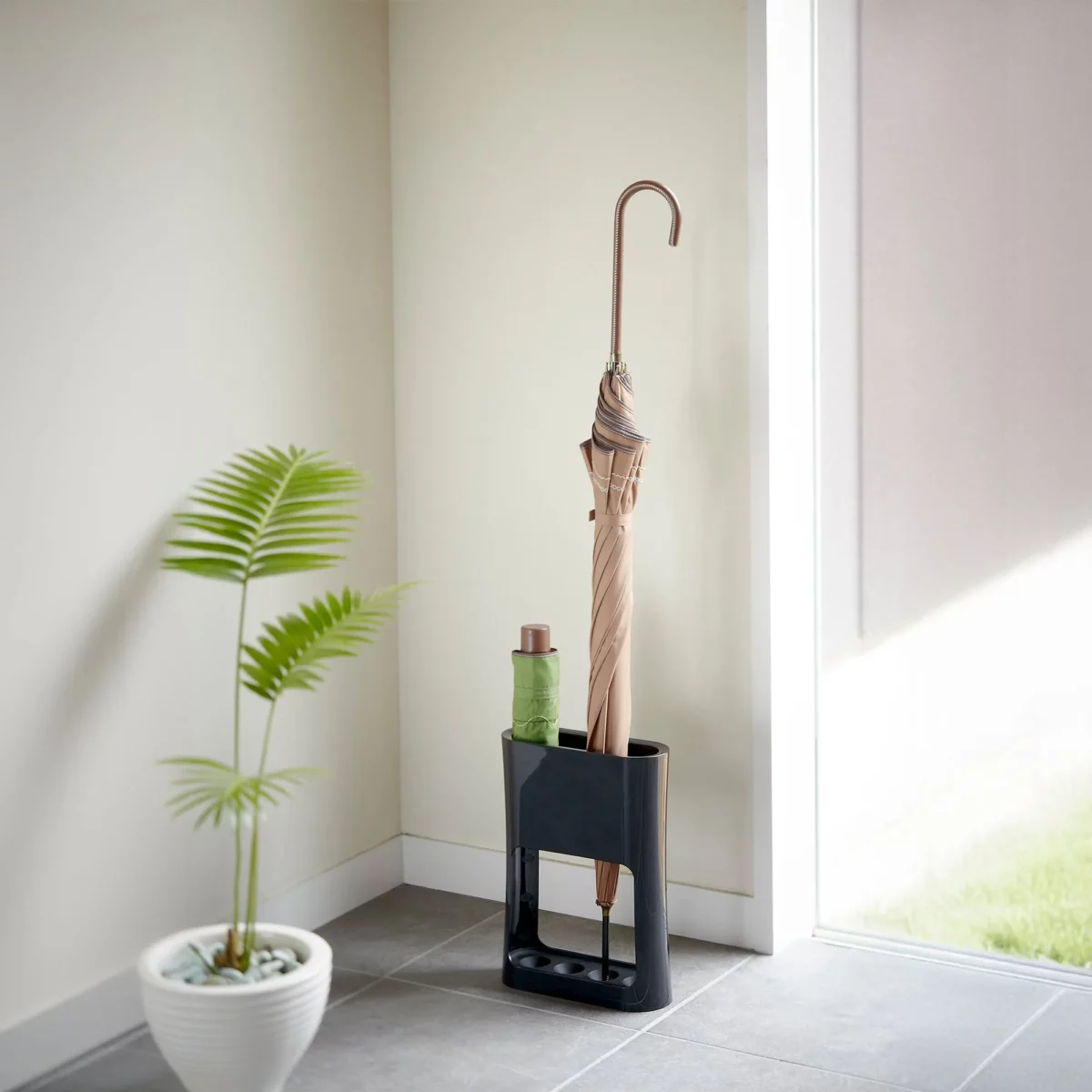 Yamazaki narrow oval umbrella stand in black, in the bright entryway next to a plant with a straight-shanked umbrella