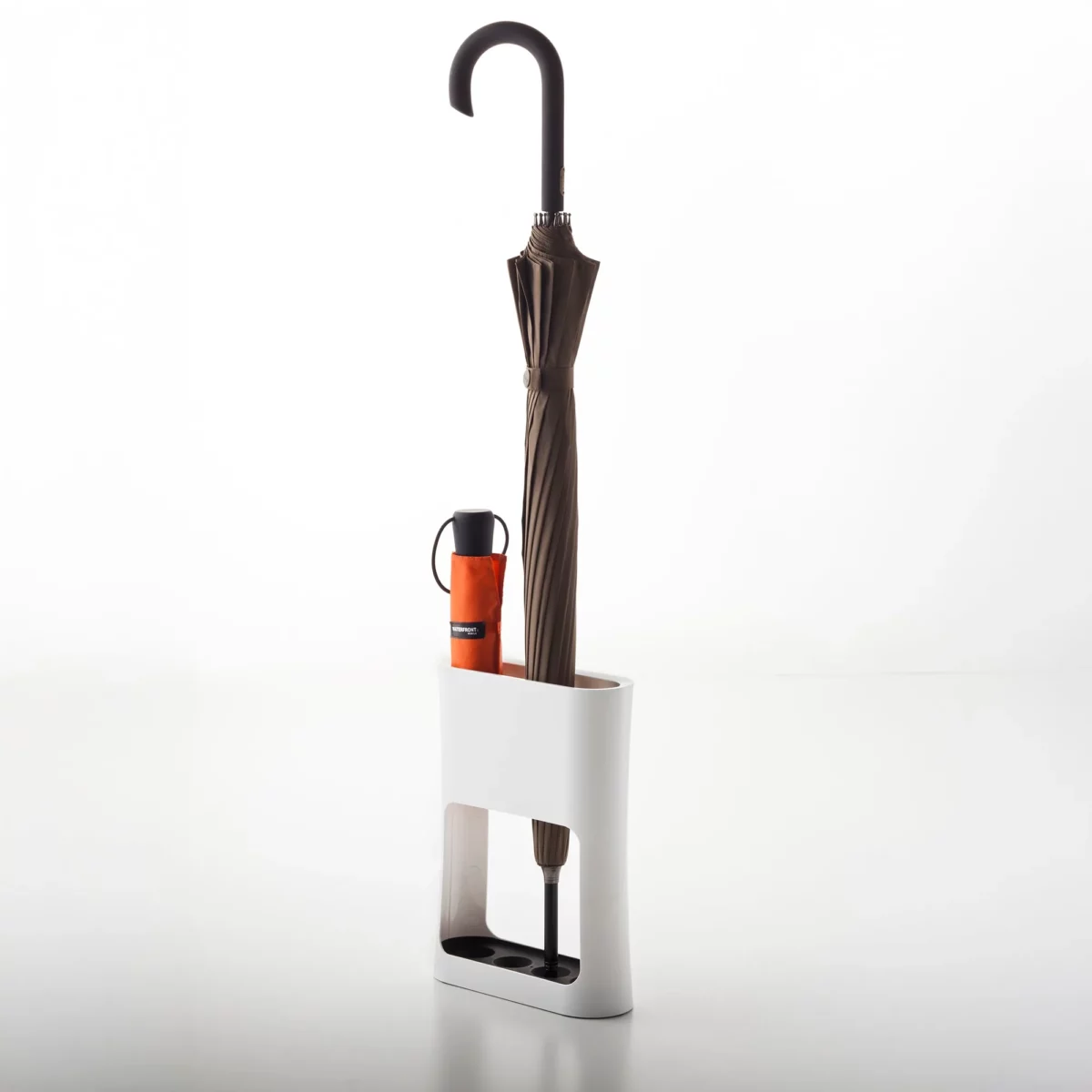 Yamazaki narrow oval umbrella stand in white, with a brown folding umbrella and an orange pocket umbrella