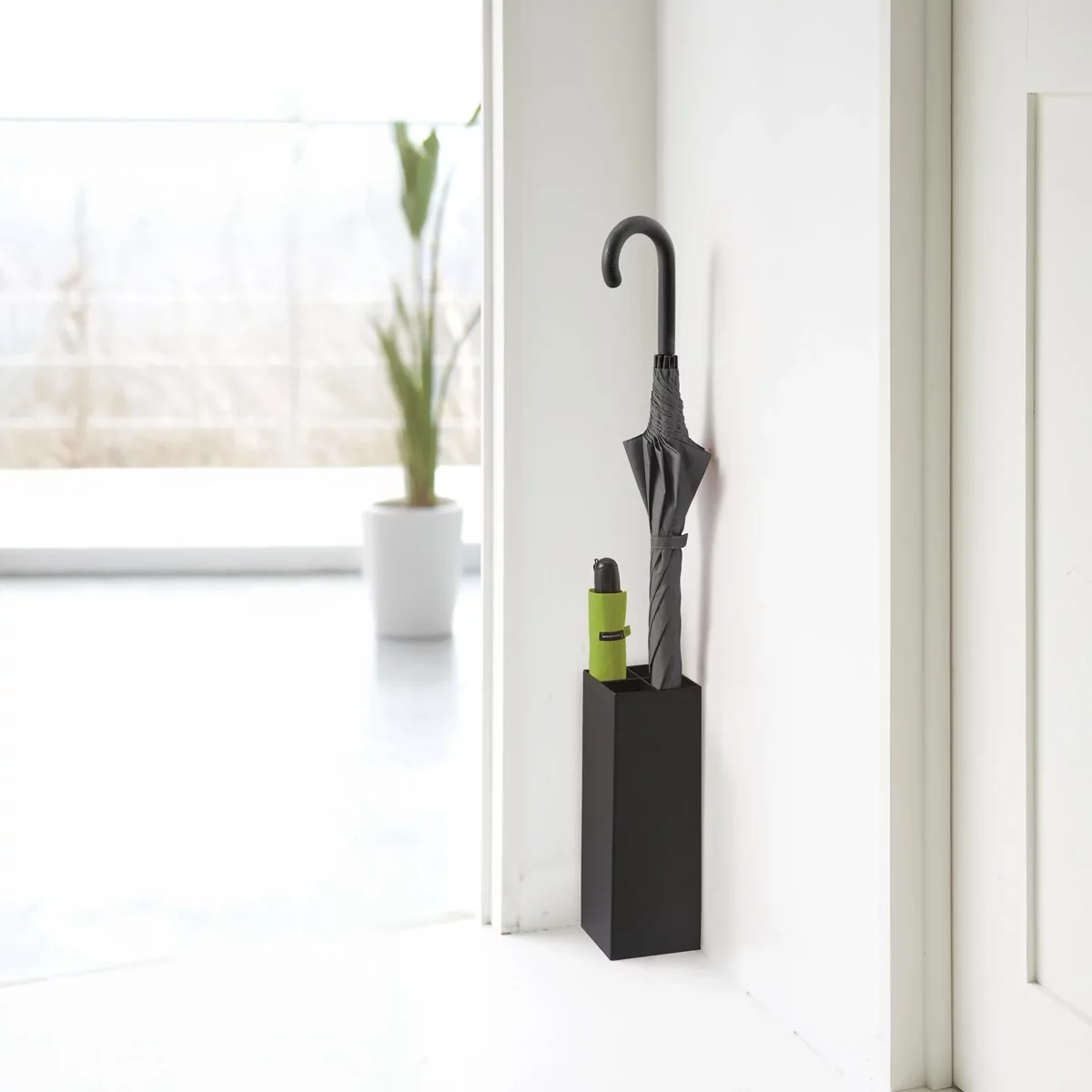 Porte-parapluies Yamazaki SMART d'angle, noir, avec un parapluie droit et un parapluie pliant vert devant la fenêtre
