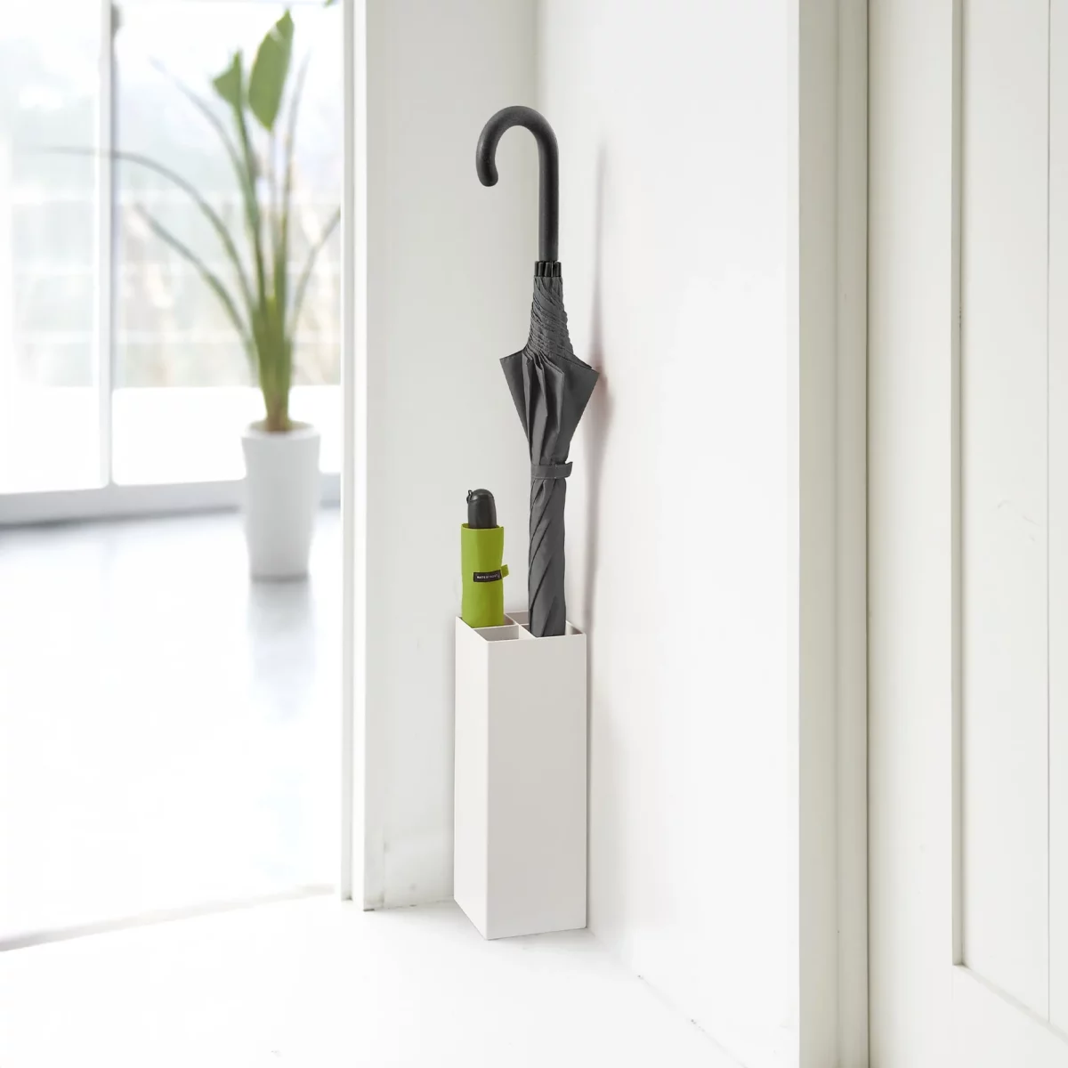 Porte-parapluies Yamazaki SMART d'angle, blanc, avec un parapluie droit et un parapluie pliant vert devant la fenêtre
