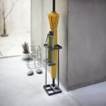 Yamazaki TOWER Slim Umbrella Stand in Black, against the concrete wall in the entryway with two umbrellas