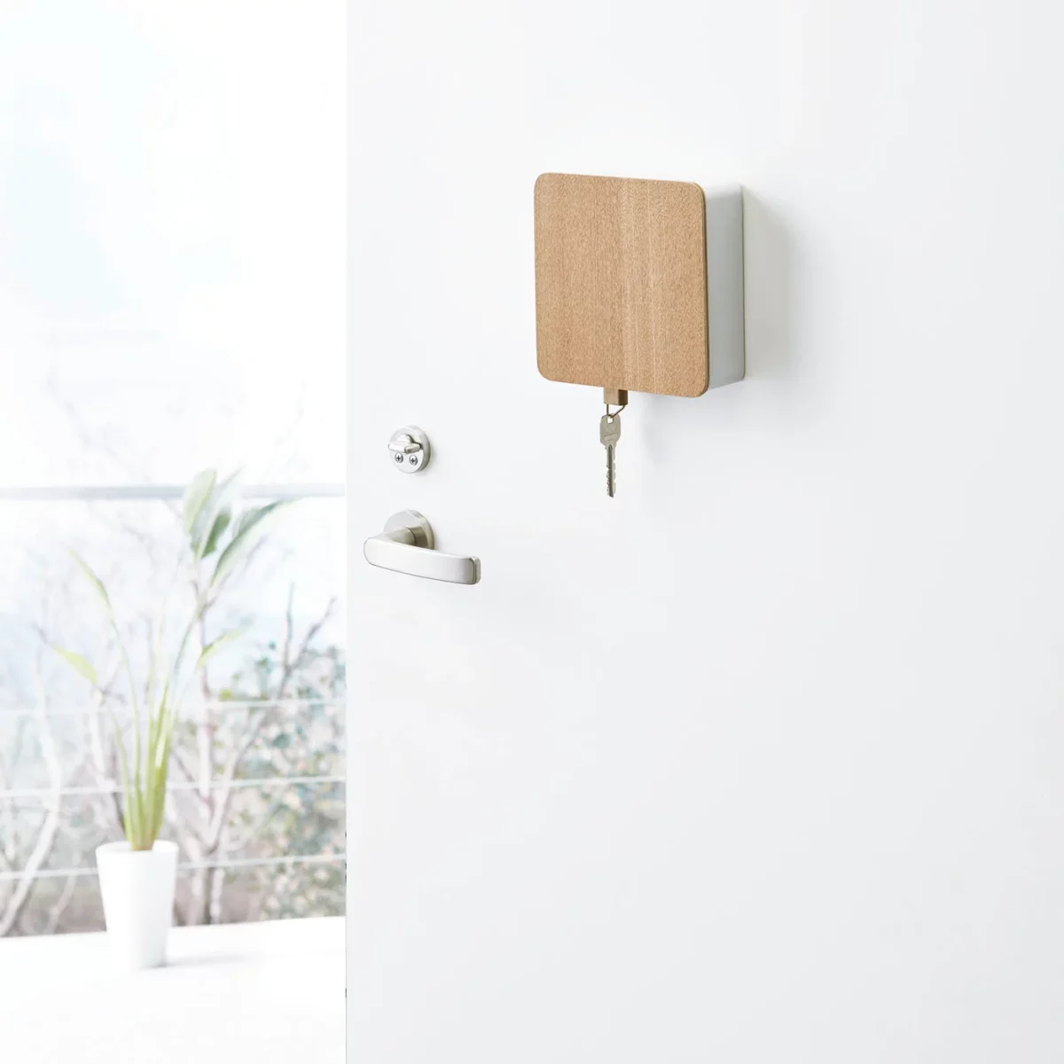 Yamazaki RIN Magnetic Key Box in White, locked on the front door, with one key hanging from the bottom
