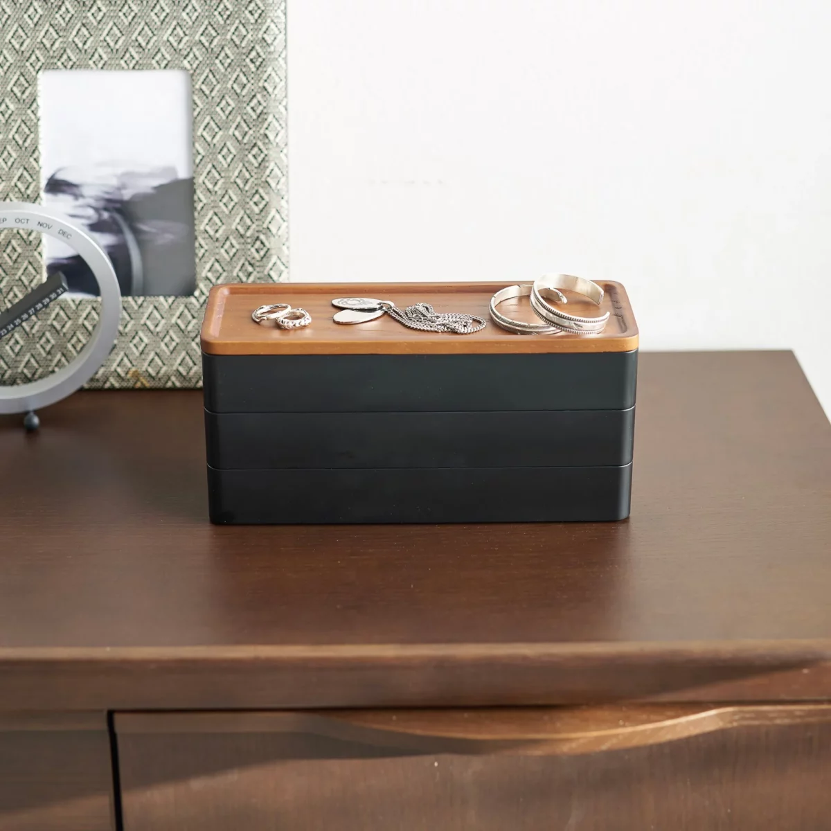 Yamazaki RIN 3-Tier Narrow Jewelry Box in Black, on the dresser in front of a picture frame