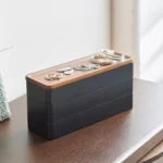 Yamazaki RIN 3-Tier Slim Jewelry Box in Black, sitting on a dresser with rings on the lid