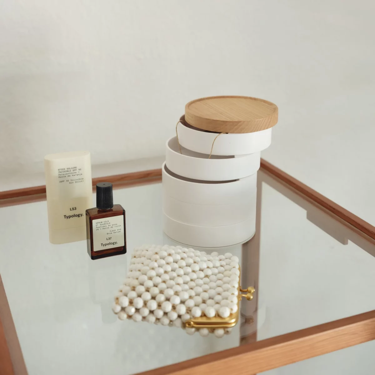 Boîte à bijoux Yamazaki TOSCA à 5 niveaux pivotants, de couleur blanche, posée sur la table en verre à côté du parfum et de la pochette à perles