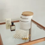 Boîte à bijoux Yamazaki TOSCA à 5 niveaux pivotants, de couleur blanche, posée sur la table en verre à côté du parfum et de la pochette à perles