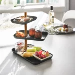 Présentoir à bijoux Yamazaki RIN à 3 étages, pivotant, de couleur noire, sur une table à manger dressée, avec des en-cas et des fruits