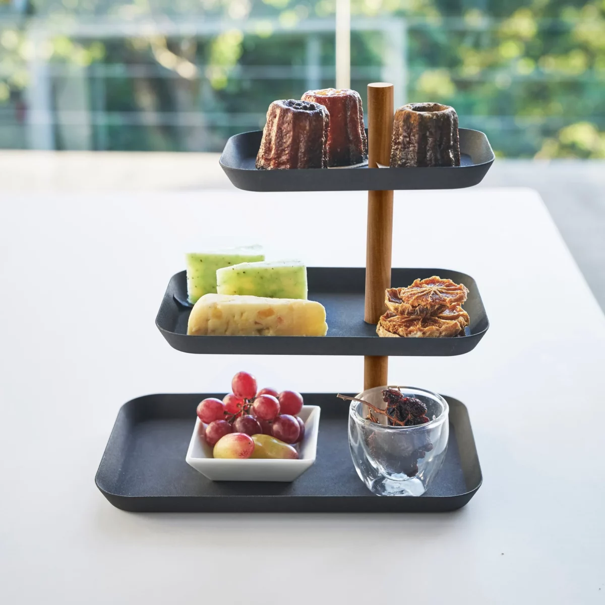 Présentoir à bijoux Yamazaki RIN à 3 étages, pivotant, de couleur noire, utilisé comme étagère avec des pâtisseries et des raisins devant la fenêtre
