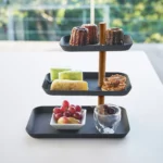 Présentoir à bijoux Yamazaki RIN à 3 étages, pivotant, de couleur noire, utilisé comme étagère avec des pâtisseries et des raisins devant la fenêtre