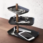 Présentoir à bijoux Yamazaki RIN à 3 étages, pivotant, de couleur noire, posé sur la commode avec des lunettes, une montre et un smartphone