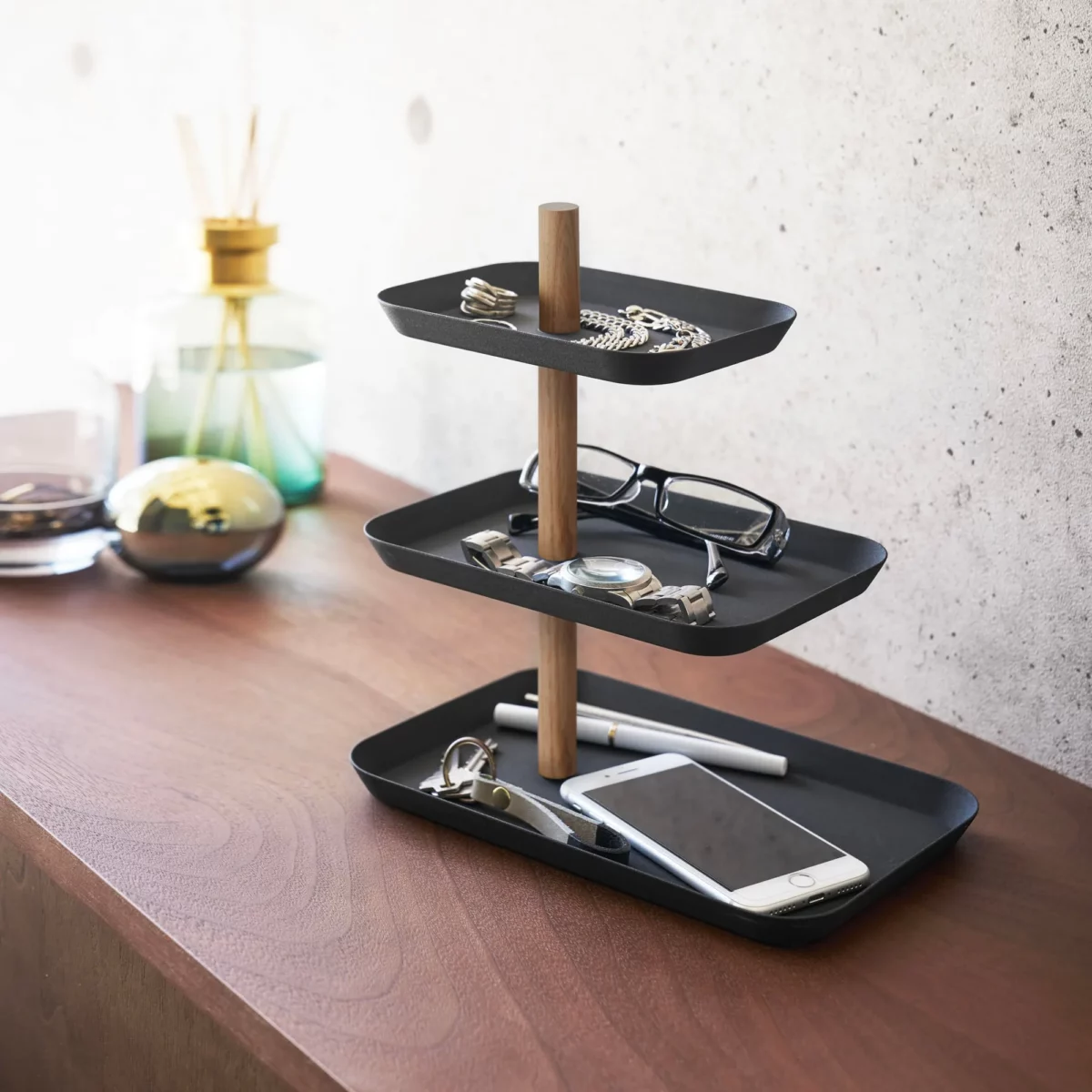 Présentoir à bijoux Yamazaki RIN à 3 étages, pivotant, de couleur noire, posé sur le buffet à côté d'un diffuseur de parfum d'ambiance