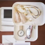 Présentoir à bijoux Yamazaki RIN à 3 étages, pivotant, de couleur blanche, avec des chaînes et une montre sur les plateaux (vu d'en haut)
