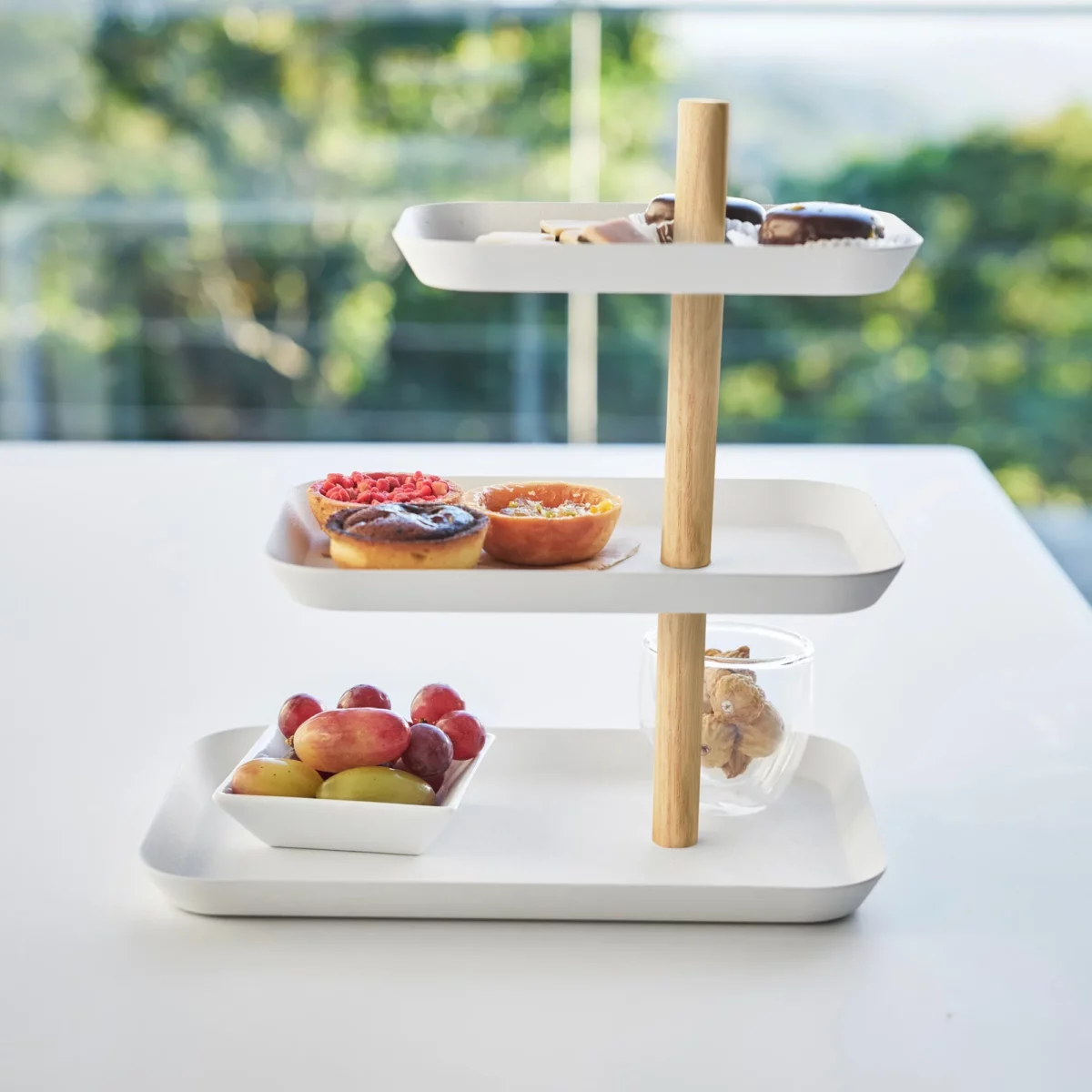 Présentoir à bijoux Yamazaki RIN à 3 étages, pivotant, de couleur blanche, avec des tartelettes et des fruits devant la vitrine