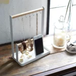 Yamazaki TOSCA Jewelry Stand with Hooks in White, placed at an angle on a wooden board with necklaces and a smartphone