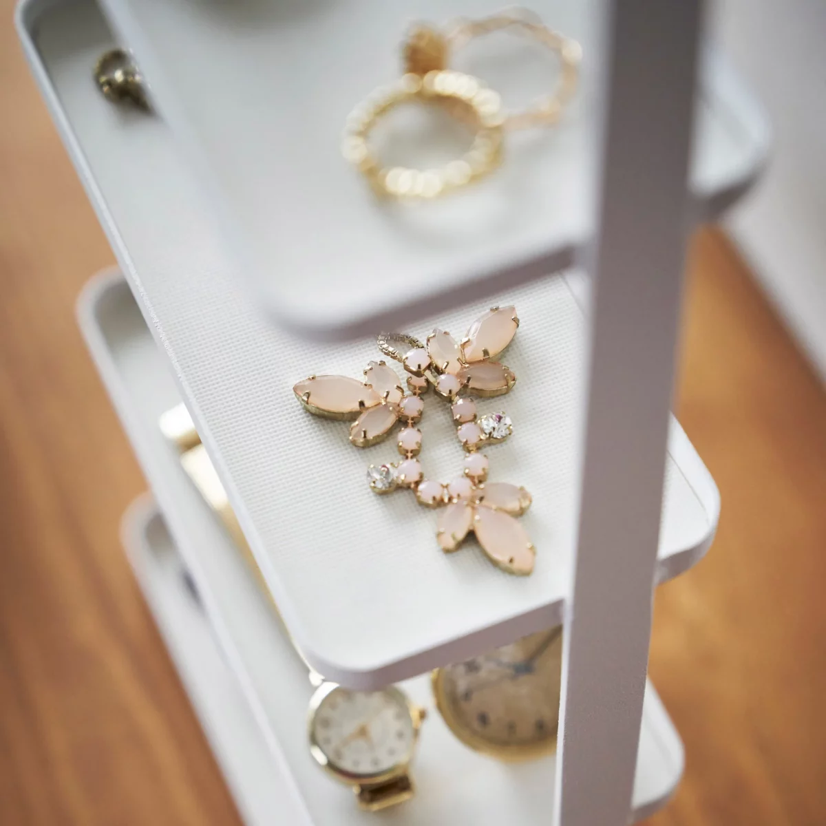 Yamazaki TOSCA 4-Tier Jewelry Stand in White, with a brooch and watch displayed on the shelves (close-up)
