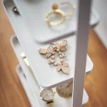 Yamazaki TOSCA 4-Tier Jewelry Stand in White, with a brooch and watch displayed on the shelves (close-up)
