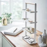 Yamazaki TOSCA 4-Tier Jewelry Stand in White, on the wooden table by the window next to a notebook