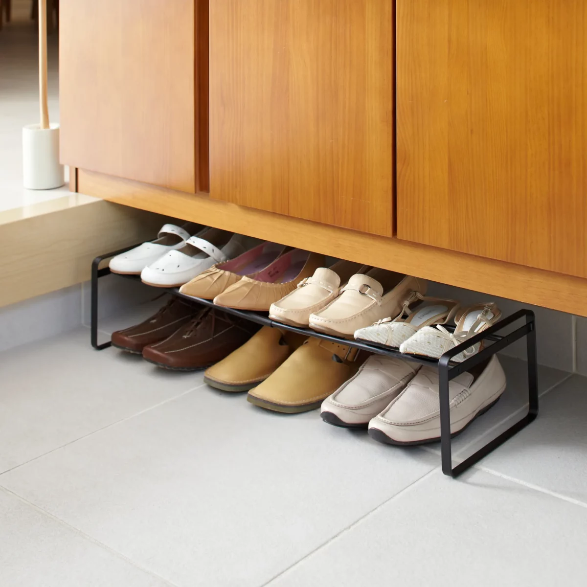 Étagère à chaussures Yamazaki FRAME extensible, de couleur noire, placée sous l'armoire d'entrée et contenant des chaussures basses et des baskets