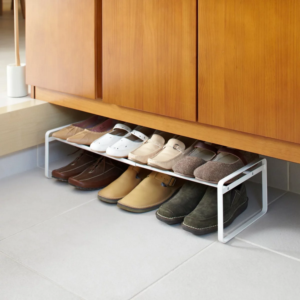Étagère à chaussures Yamazaki FRAME extensible, blanche, placée sous l'armoire d'entrée et contenant des chaussures basses et des baskets