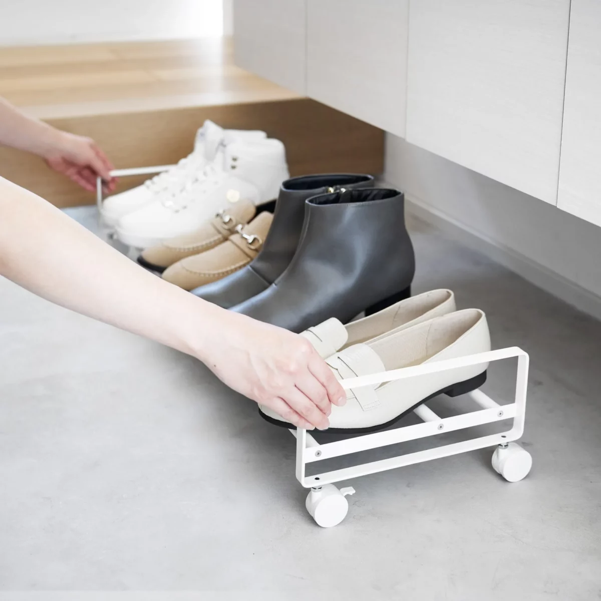 Yamazaki Schuhregal TOWER mit Rollen in Weiss, Hand zieht das Regal unter dem Schrank hervor