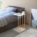 Table basse PLAIN de Yamazaki, en blanc, utilisée comme table de chevet à côté du lit, avec un livre et un réveil