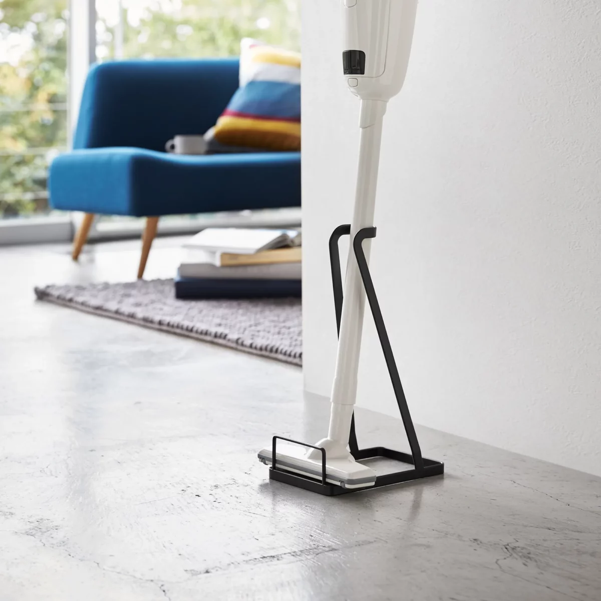 Yamazaki Staubsaugerständer TOWER in Schwarz, mit Stielstaubsauger im Wohnzimmer neben dem Sofa