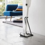 Yamazaki Staubsaugerständer TOWER in Schwarz, mit Stielstaubsauger im Wohnzimmer neben dem Sofa