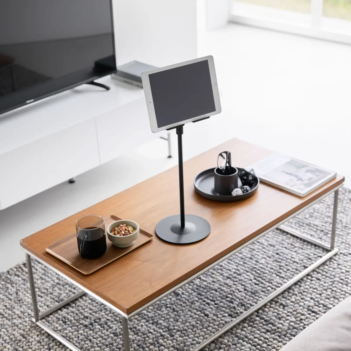 Support pour tablette Yamazaki SMART, réglable en hauteur, de couleur noire, posé sur la table basse devant la télévision