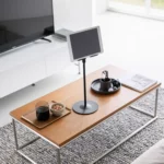 Support pour tablette Yamazaki SMART, réglable en hauteur, de couleur noire, posé sur la table basse devant la télévision