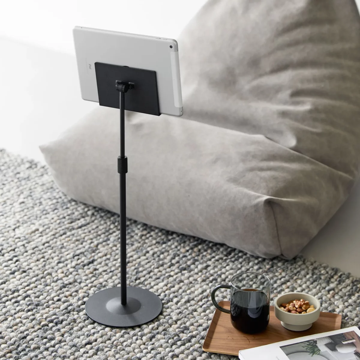 Support pour tablette Yamazaki SMART, réglable en hauteur, de couleur noire, posé au sol à côté du pouf avec tablette