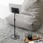 Support pour tablette Yamazaki SMART, réglable en hauteur, de couleur noire, posé au sol à côté du pouf avec tablette