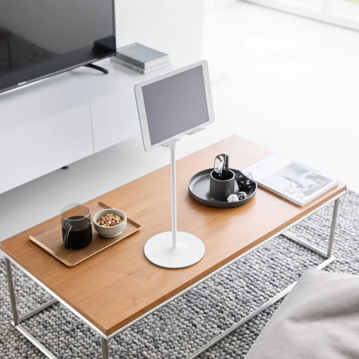 Support pour tablette Yamazaki SMART, réglable en hauteur, de couleur blanche, posé sur la table basse devant la télévision