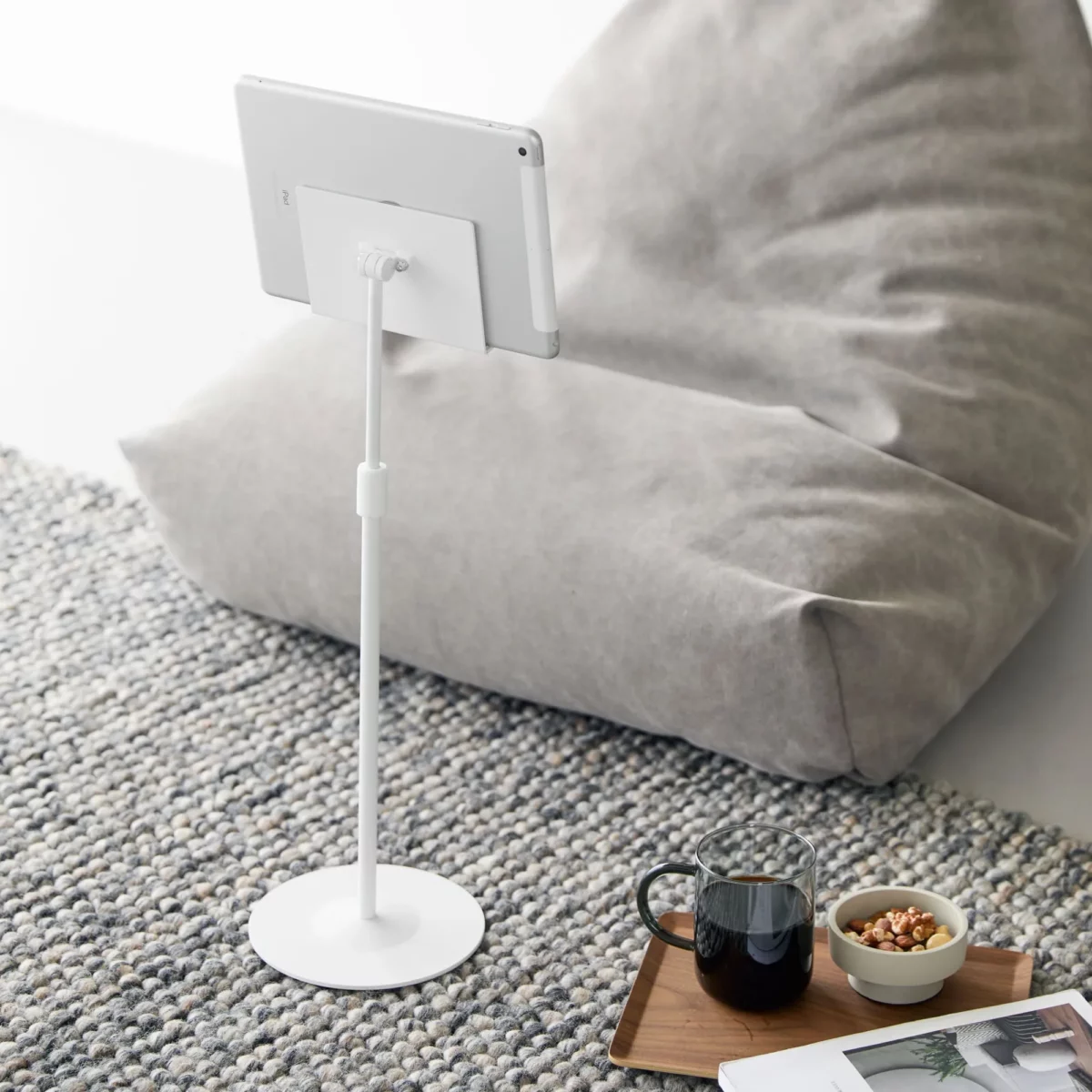 Support pour tablette Yamazaki SMART, réglable en hauteur, de couleur blanche, posé au sol à côté du pouf avec tablette
