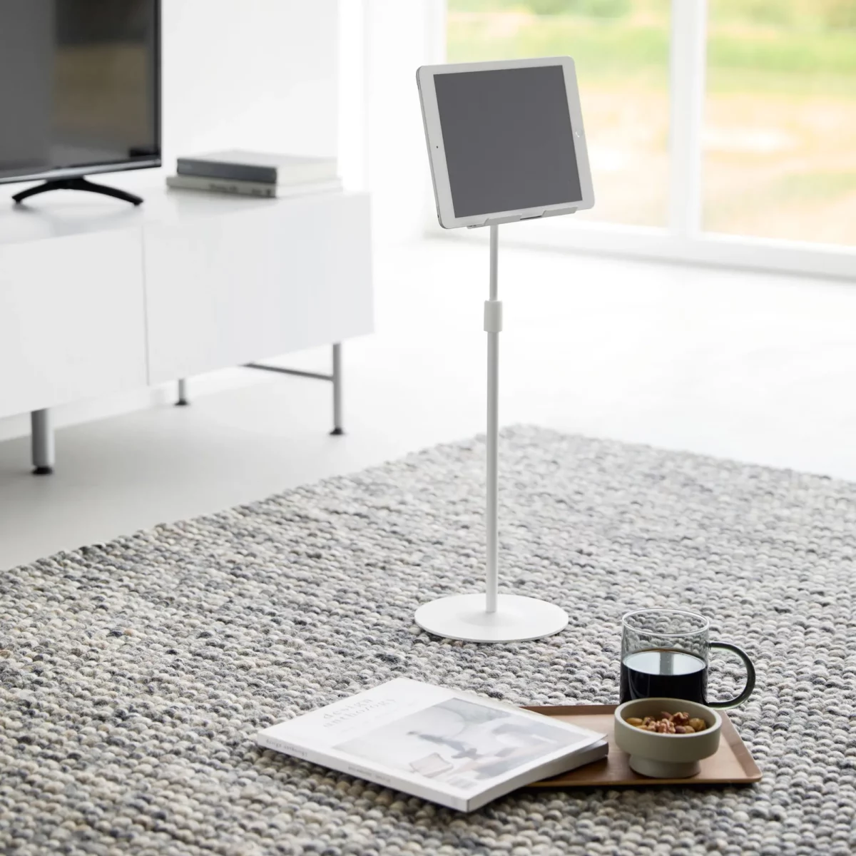Support pour tablette Yamazaki SMART, réglable en hauteur, de couleur blanche, posé au sol dans le salon, à côté d'un magazine et d'un thé