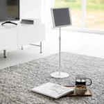 Support pour tablette Yamazaki SMART, réglable en hauteur, de couleur blanche, posé au sol dans le salon, à côté d'un magazine et d'un thé